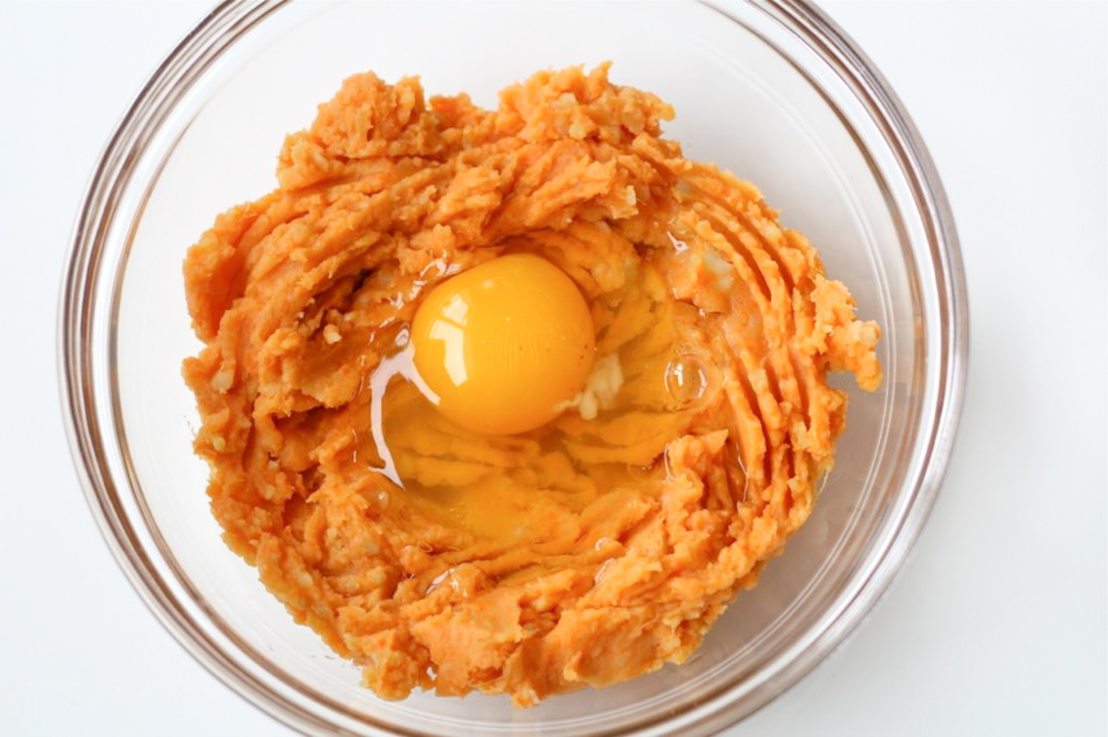 bowl of mashed sweet potatoes with a raw egg on top