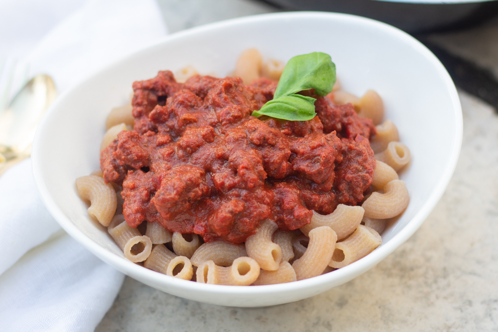 a bowl of pasta with bolognese sauce and basil